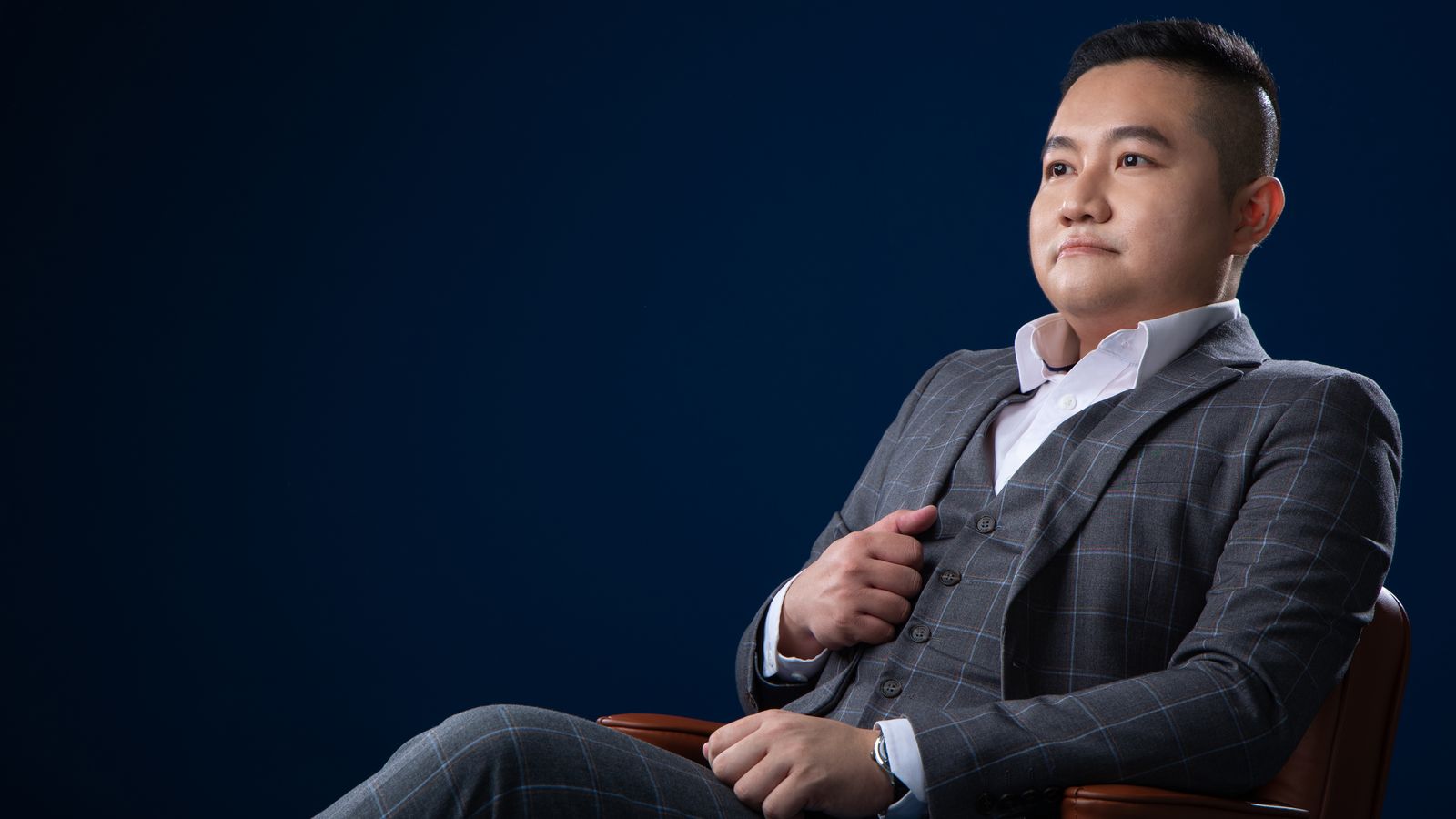 Kevin Lee, REN 14973, seated in a grey suit against a deep blue backdrop